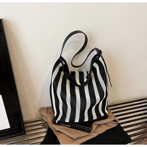 Detail view of a black and white striped mesh tote bag with a sleek leather shoulder strap