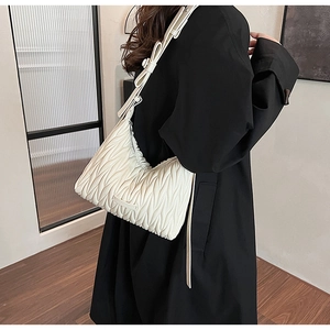 Detail of white pleated underarm bag with matelasse texture shown on a model shoulder