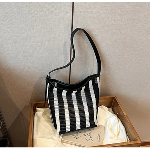 Detail of striped mesh shoulder bag with black leather trim on a wooden tray