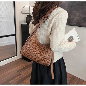 Detailed view of caramel brown pleated underarm bag with decorative bow and logo