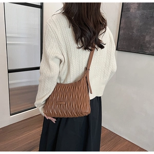 Detail of a brown quilted hobo bag featuring vertical pleats and an adjustable shoulder strap