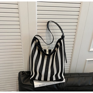 Detail view of black and white striped mesh tote bag with leather strap on leather sofa