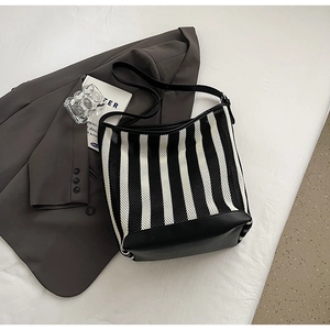Close-up of black and white striped shoulder bag on a grey blazer with fashion props