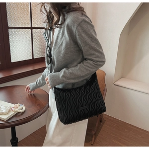 Detail of black pleated crossbody bag with premium leather texture on a female model