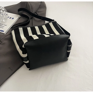 Detail of black and white striped woven tote bag with leather trim on white background
