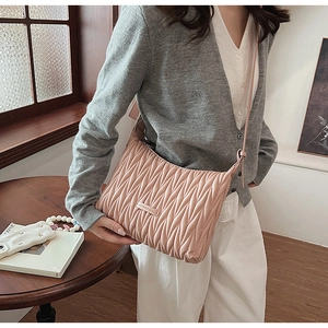 Detail of pink matelassé shoulder bag with metal logo and pleated leather texture