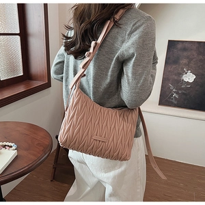 Detail of pink pleated crossbody bag with ribbon knot and brand tag on a model