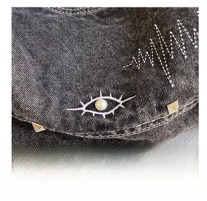 Detailed close-up of eye embroidery with pearl and metal studs on grey denim tote