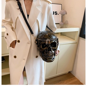 Detailed bronze skull crossbody bag with realistic texture and double zipper on beige coat