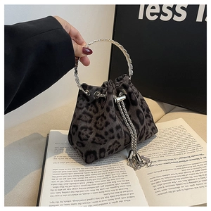 Close-up of leopard bucket bag with metal ring handle and chain tassel detail on a book