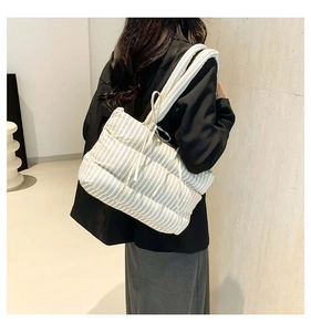 Détail d'un grand sac cabas matelassé à rayures porté à l'épaule par un mannequin en salle