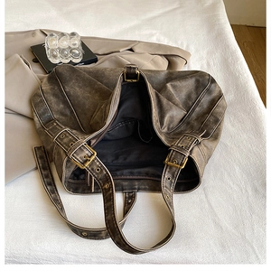 Detail of vintage washed PU leather shoulder bag with bronze buckles on white sheets