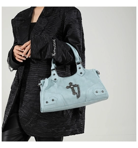 Detail der hellblauen Punk-Tasche mit silbernem Kreuzanhänger und Nieten auf dunklem Anzug
