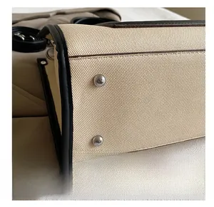 Detailed close-up of durable beige canvas handbag bottom with black leather trim and silver studs