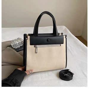 Detail of canvas tote bag showing black leather trim and detachable shoulder strap