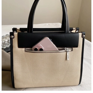 Detail of minimalist beige canvas tote bag with black leather trim and front zip pocket