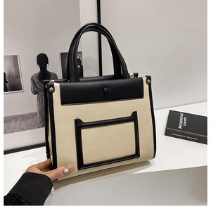 Detailed view of large beige canvas tote bag with black leather trim and pocket detail