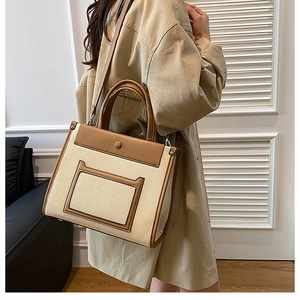 Detail of a large capacity two-tone tote bag with brown leather trim shown on model