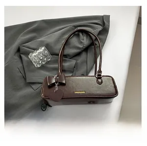 Detail of deep brown baguette bag with gold logo and heart-shaped bow charm