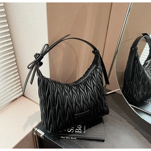 Detail of black pleated hobo bag with matelassé texture and bow accent on the strap