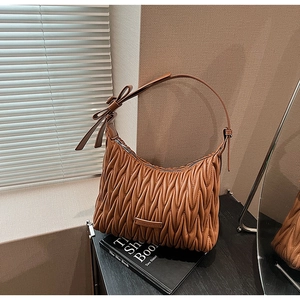 Detailed view of brown pleated faux leather shoulder bag with decorative bow and silver hardware