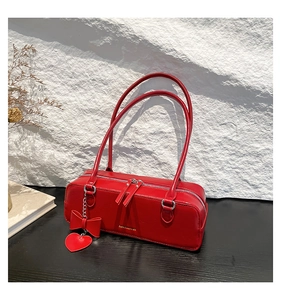 Detail of red leather baguette bag with heart charm and gold logo on textured background