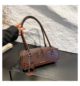 Close-up of brown leather bag with golden logo and decorative bow charm detail