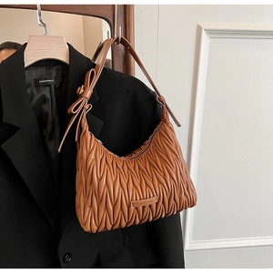 Detail of a brown pleated shoulder bag with bow decor hanging on a black suit jacket