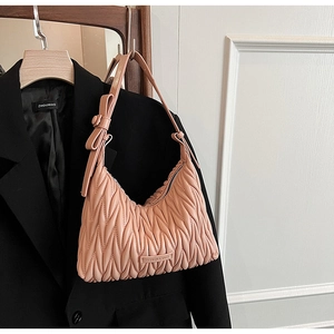 Detailed view of pink pleated shoulder bag with bow strap and metallic logo plaque