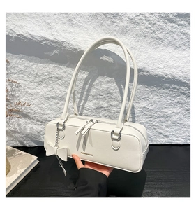 Close-up of white minimalist baguette bag with gold lettering and bow charm detail