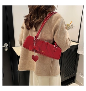 Red glossy baguette bag with bow detail and heart charm shown on model shoulder