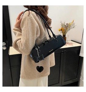 Detail of black faux leather shoulder bag with chic bow and heart charm on a metal chain