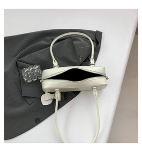 Close-up of cream rectangular shoulder bag with heart pendant on grey blazer