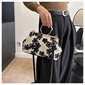 Détail du sac vintage à fermoir avec broderie florale noire et blanche et poignée dorée