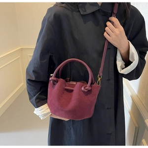 Detail of burgundy suede bucket bag with rigid handle and side knot worn by a model