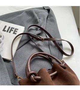 Detail of a brown matte suede bucket bag with knotted handle and adjustable strap