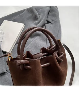 Close-up of brown suede bucket bag with knotted leather handle on a grey blazer