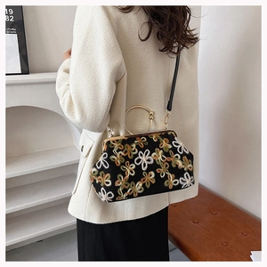 Détail de la broderie florale et de l'anse dorée circulaire sur le sac de soirée coquillage