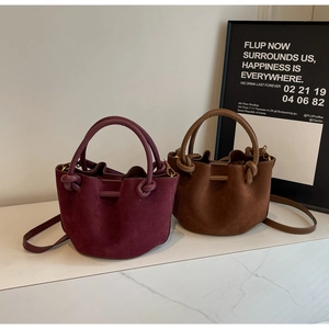 Detail of burgundy and brown suede drawstring bucket bags with round handles and gold hardware