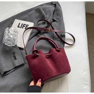 Detail of burgundy matte suede bucket bag with knotted handle and brass hardware