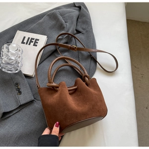 Detail of a brown frosted suede bucket bag with knotted handle and leather base