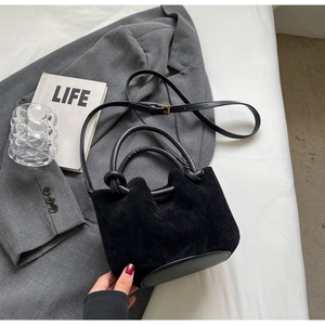 Detail of black suede bucket bag with round leather base and gold-tone hardware accents