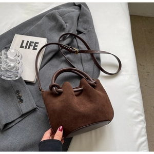 Detail of dark brown matte suede bucket bag with round handle on grey suit fabric