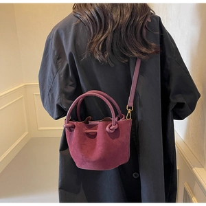 Detail view of burgundy frosted suede bucket bag with round handle on a black coat