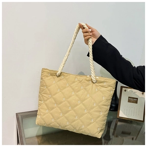 Detail of beige quilted tote bag featuring white bow embroidery and thick rope handle