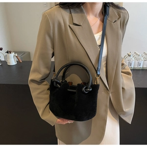 Macro view of a black matte suede bucket bag with round handles and a detachable strap