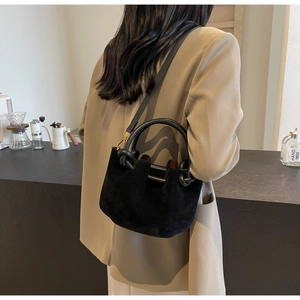 Detail of black suede bucket bag with knotted handle and detachable shoulder strap