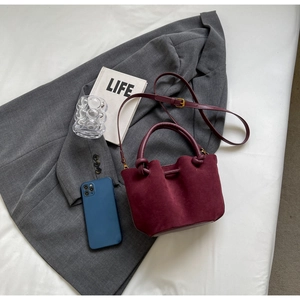 Detail of burgundy suede bucket bag with knotted handle and adjustable strap
