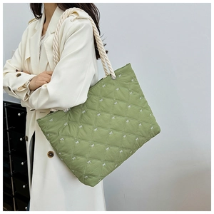 Detail of green quilted tote bag with embroidered bows and woven rope shoulder strap