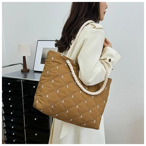 Detailed close-up of brown quilted canvas tote bag with white bow embroidery and rope handle